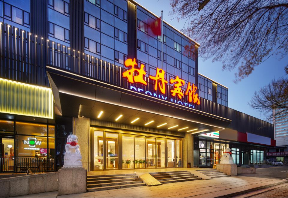 The hotel in an urban setting has a front view and entrance featuring large glass panels at Peony Hotel(Mudanyuan Subway Station)