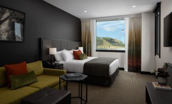 a modern hotel room with a large bed , couch , and window overlooking a mountainous landscape at Rydges Wellington Airport, an EVT hotel