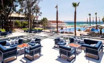 a patio area with multiple lounge chairs and tables , overlooking the ocean , and palm trees at Potidea Palace Hotel