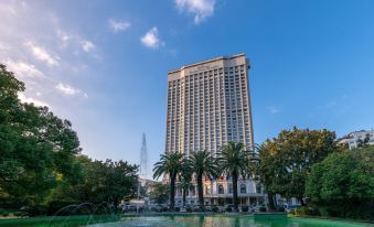 A large building with trees in front and the sky behind it, featuring a clear blue sky above at Okura Garden Hotel Shanghai