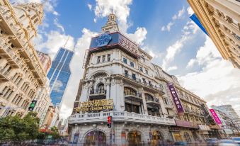 There is a large building with people on the street in front and another tall skyscraper behind it at Yitel Premium (Shanghai people's Square Nanjing Road Pedestrian Street shop)