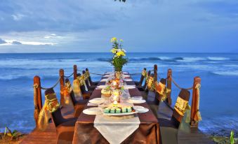 a large dining table set up for a formal dinner on the beach , with multiple chairs arranged around it at Mambruk Hotel & Convention