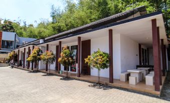 a row of trees and flowers in front of a white building with columns , creating a picturesque scene at Bwalk Hotel Malang