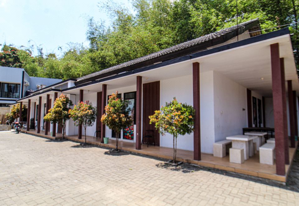 a row of white buildings with red pillars , green trees , and flowers in front of them at Bwalk Hotel Malang