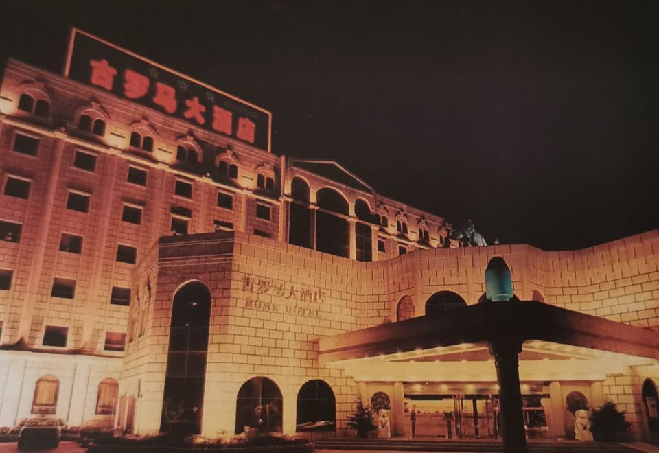 a large building with a sign on it is illuminated at night , and a person stands nearby at Rome Hotel