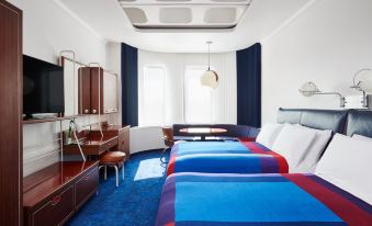 a modern hotel room with two beds , a desk , and a small kitchenette , all decorated in blue and red colors at The Standard London