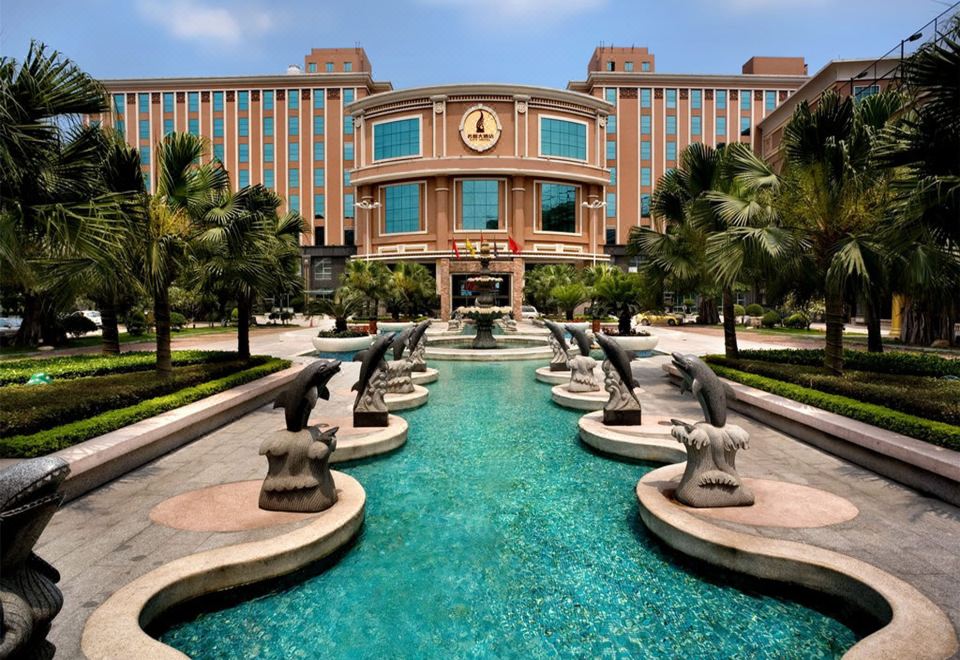 a large hotel with a pool and fountain in front of it , surrounded by palm trees at City Hotel