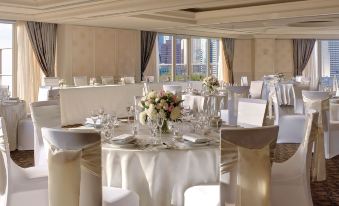 a large , elegant dining room with multiple round tables set for a formal event , complete with white tablecloths and centerpieces at The Langham Melbourne