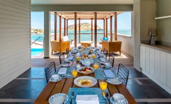 a long wooden table with plates , cups , and cutlery set for breakfast on a balcony overlooking the ocean at Park Hyatt St Kitts Christophe Harbour