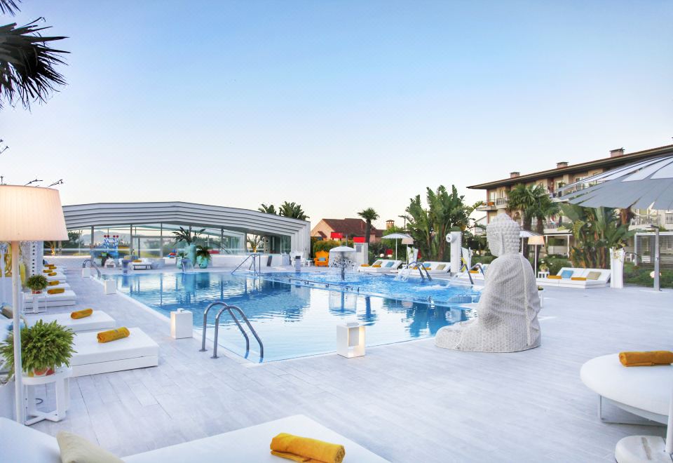 a large outdoor pool surrounded by lounge chairs and umbrellas , with palm trees in the background at Augusta Eco Wellness Resort 4 - SPA Access included