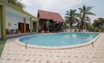 a large swimming pool is surrounded by a house and palm trees , with a tiled patio in front of it at Bwalk Hotel Malang