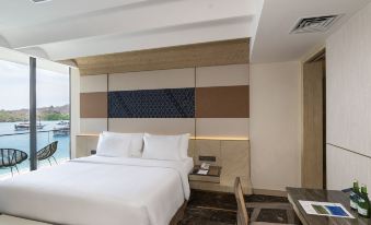 a modern hotel room with a white bed , wooden furniture , and a large window offering a view of the city at Meruorah Komodo Labuan Bajo