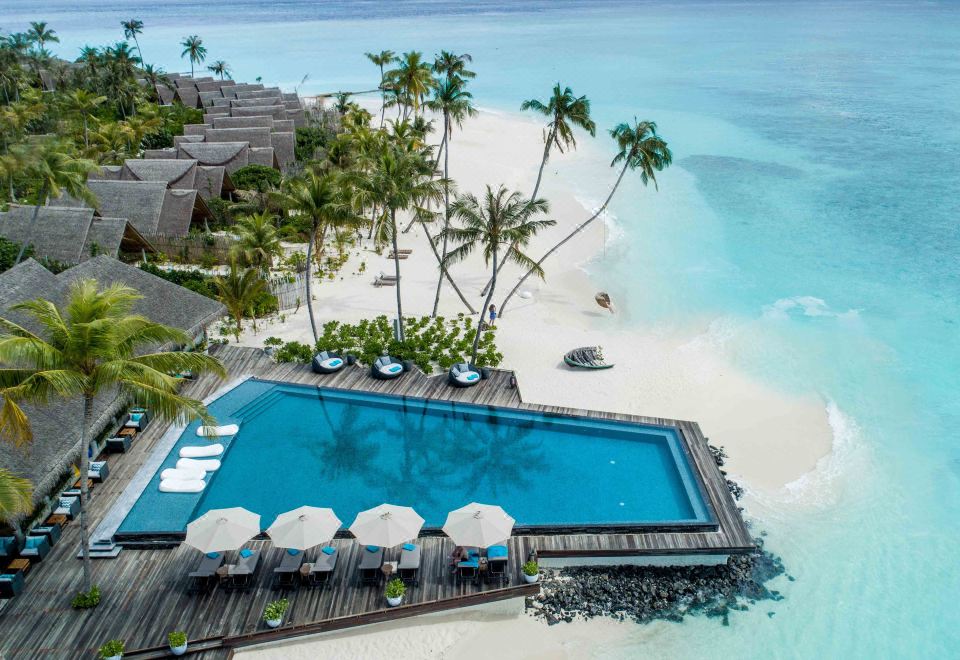 an aerial view of a resort with a large swimming pool surrounded by palm trees and beach chairs at Fushifaru Maldives