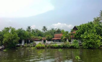 a body of water with several houses on the shore , creating a picturesque scene at Parn Dhevi Riverside Resort & Spa