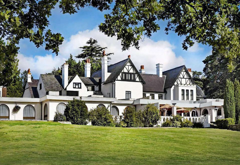 a large white house surrounded by trees and grass , with a large tree in the background at Hilton Cobham