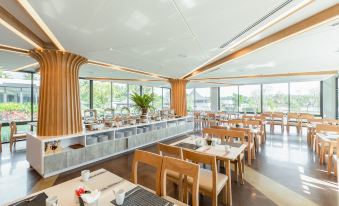 a modern restaurant with wooden tables and chairs , a bar , and large windows overlooking the city at Na Tree Tara Riverside Resort Amphawa Damnoensaduak