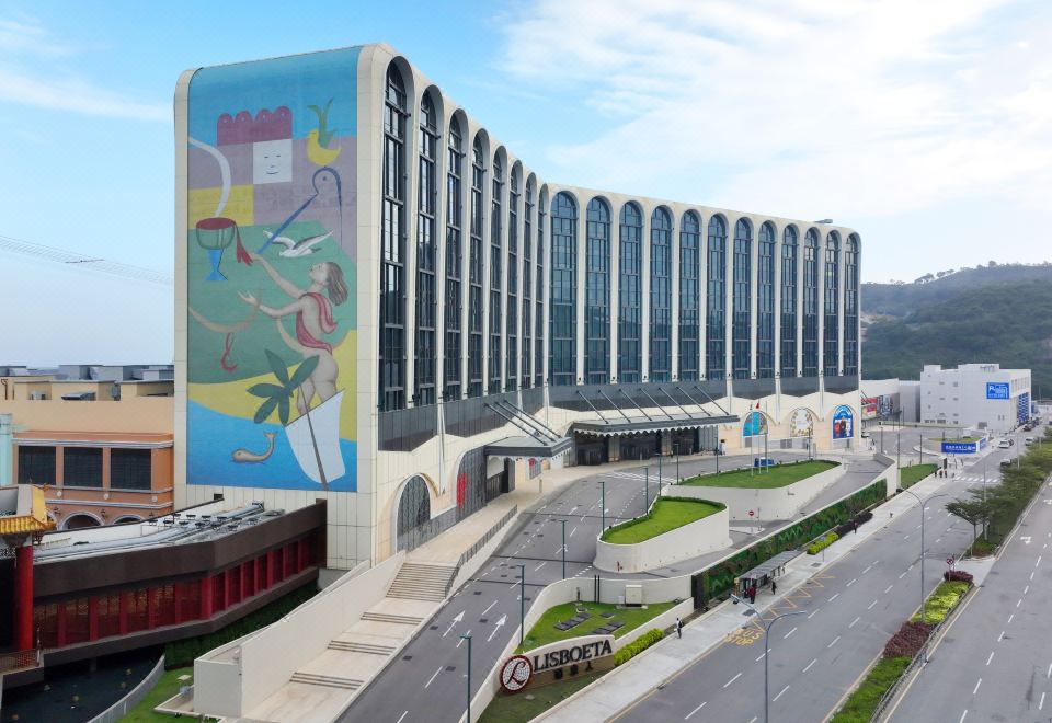 A large building with an umbrella in front and another hotel on the other side at Lisboeta Macau