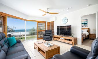 a spacious living room with a large flat - screen tv mounted on the wall , surrounded by couches and chairs at Rolling Surf Resort Sunshine Coast