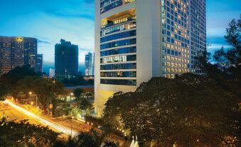 a tall building with a blue and white facade is surrounded by trees and other buildings at Hotel Maya Kuala Lumpur City Centre