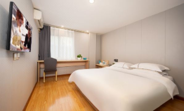 A modern bedroom with a large window, a white bed, and a wooden desk in the center at Seven Orange Hotel (Guangzhou Railway Station)