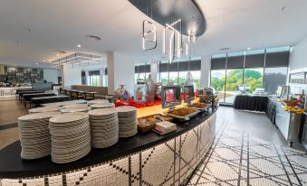 a buffet table with plates , a hot plate , and various dishes is displayed in a room with large windows at Travelodge Ipoh