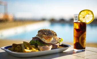 a plate of food with a burger , fries , and a glass of water on a table near a pool at Hotel Colombo