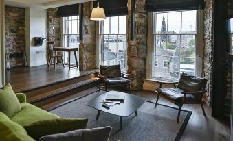 a modern living room with large windows , stone walls , and green furniture , including armchairs , coffee table , and dining table at Old Town Chambers, Autograph Collection