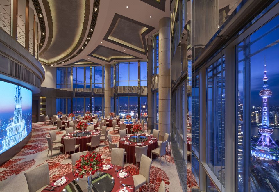 A restaurant with large windows and floor-to-ceiling glass offers a picturesque view of the city at dusk at Grand Hyatt Shanghai