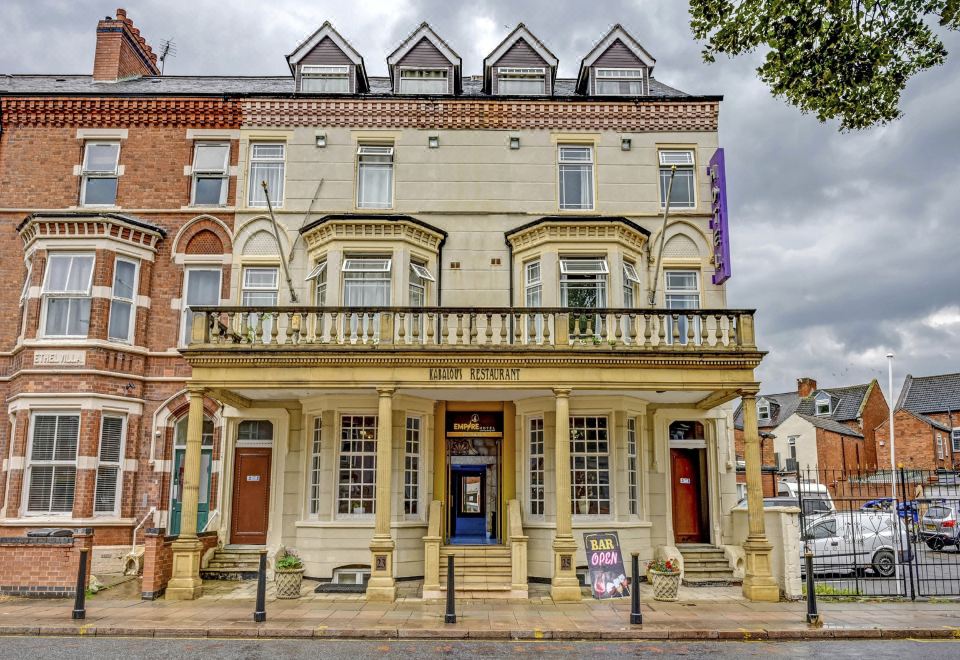 a large , white building with a balcony on the second floor and a blue door in front of it at Empire Hotel