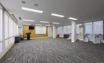 A large room with white walls and carpeted flooring contains an empty meeting space at Shanghai Jinjiang Metropolo Classic East Nanjing Road Hotel