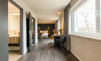 a modern hotel room with hardwood floors , a double bed , and a bathroom visible through an open door at Maseven München Messe Dornach