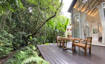 a wooden deck surrounded by lush greenery , with a dining table and chairs placed on the deck at Proud Phu Fah Maerim Resort