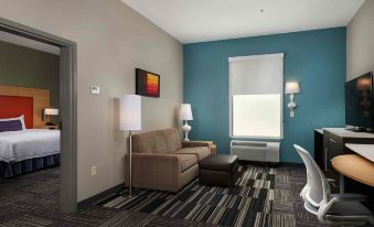 a modern living room with a couch , coffee table , and desk in a hotel room at Home 2 Suites by Hilton Muskogee