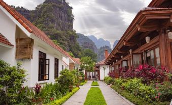 a picturesque village with white buildings , green grass , and a path leading to the mountains at Tam Coc La Montagne Resort & Spa