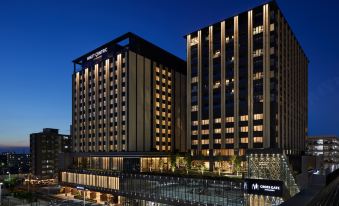 At night, there is a hotel in the foreground with an illuminated building behind it at Hyatt Centric Kanazawa