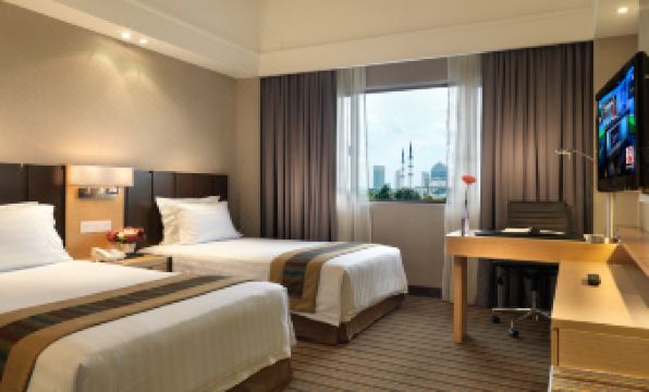 a hotel room with two beds , a desk , and a window , all decorated in neutral colors at Concorde Hotel Shah Alam
