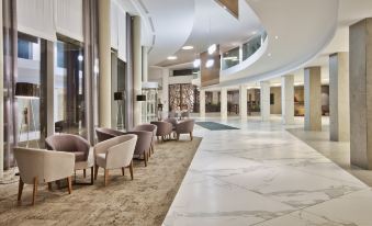 a modern hotel lobby with marble floors and white walls , featuring several chairs and couches arranged in the space at DoubleTree by Hilton Malta