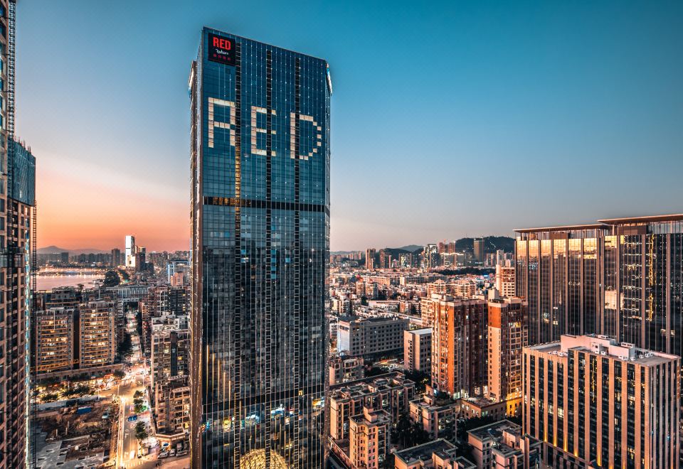 A city with tall buildings and large windows is illuminated by the setting sun at Radisson RED Hotel Zhuhai Gongbei Port