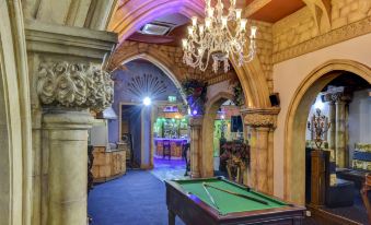 a billiards table in a dimly lit room with stone arches , a chandelier , and a clock on the wall at Empire Hotel