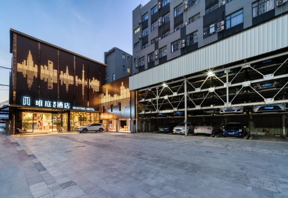 In front of an overcast sky, there is a hotel entrance with a parking lot and additional buildings at Weiting Century Hotel