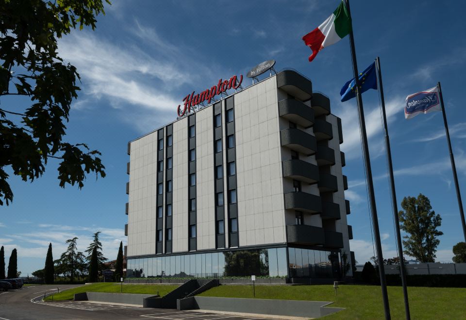 "a large white building with the name "" champin "" prominently displayed on top , surrounded by flags and trees" at Hampton by Hilton Rome North Fiano Romano