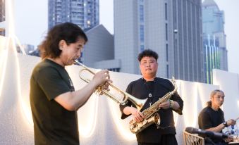 A man is playing the saxophone while another person is playing a different musical instrument in front of him at Grand Madison Wuhan Hankou on the Bund