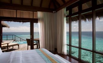 a bedroom with a bed and sliding glass doors leading to a balcony overlooking the ocean at Coco Bodu Hithi