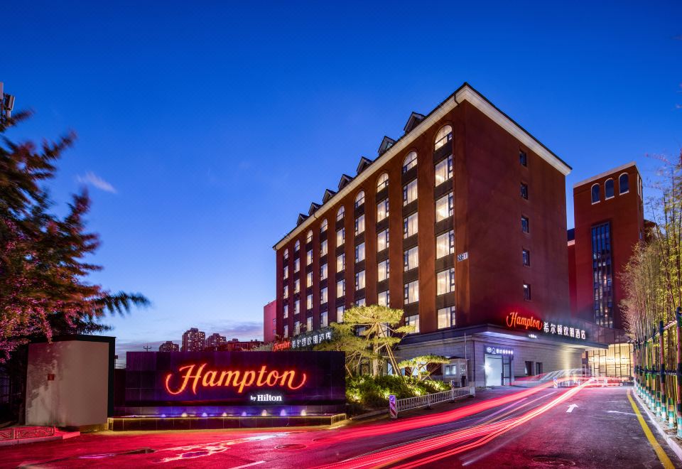 At night, there is an illuminated sign on top of a hotel, with a view of the exterior in front at Hampton by Hilton Beijing Guomao CBD