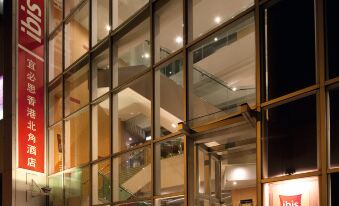 At night, the front entrance of a hotel is reflected in windows, with an illuminated sign at Ibis Hong Kong North Point