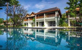 a large , two - story house with a red roof and white walls is reflected in the blue water below at Grand Mercure Khao Lak Bangsak