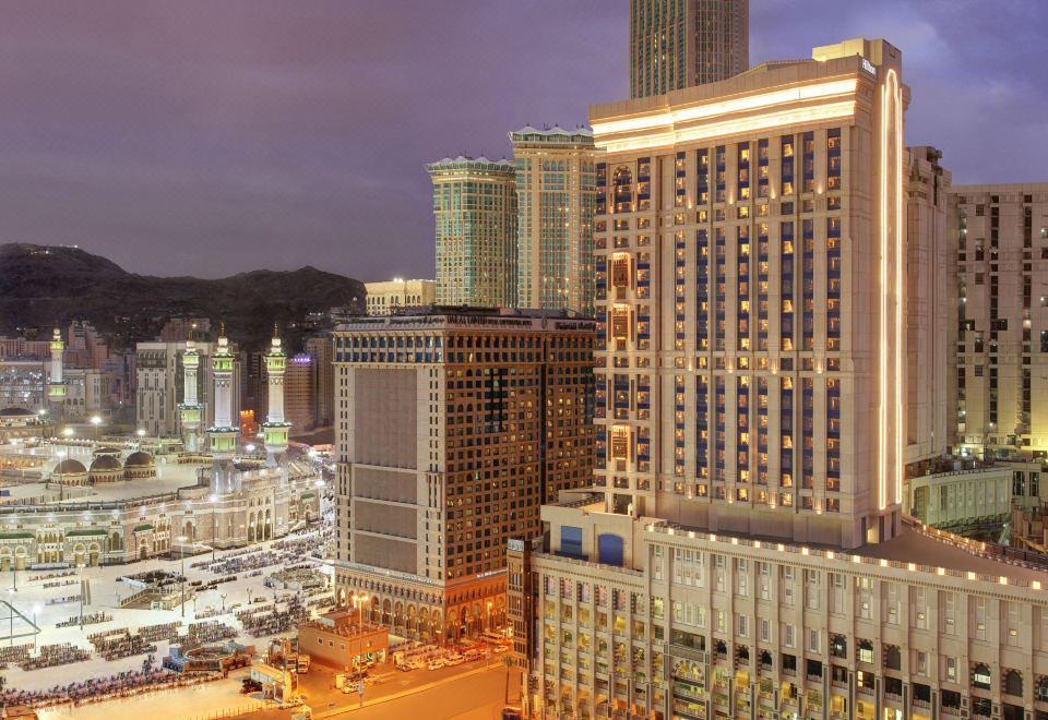 a large city skyline at night , with tall buildings lit up and a clear blue sky at Hilton Suites Makkah