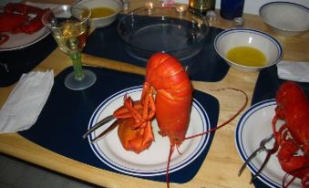 a large red lobster is placed on a white plate , surrounded by various dishes and utensils on a wooden table at Chisholms of Troy Coastal Cottages