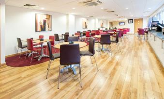 a large , empty conference room with wooden floors and tables , red chairs , and white walls at Travelodge London Chessington Tolworth