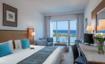 a hotel room with a large bed , desk , and a view of the ocean through sliding glass doors at Mediterranean Beach Hotel